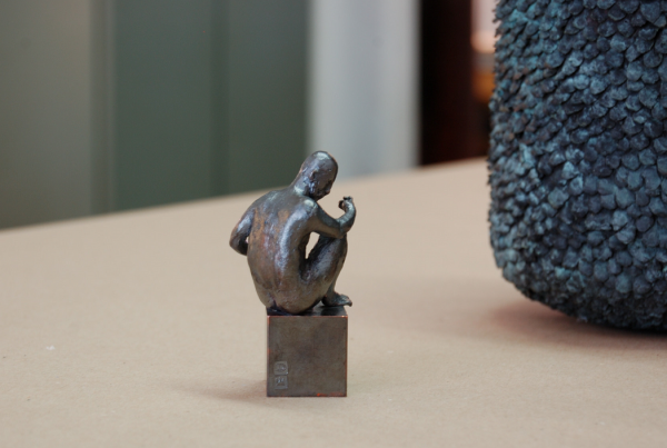 Rückenansicht einer kleinen männlichen Figur aus Bronze auf einem Sockel sitzen